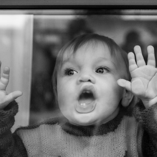 klein kind drukt zijn gezicht en handen tegen het raam